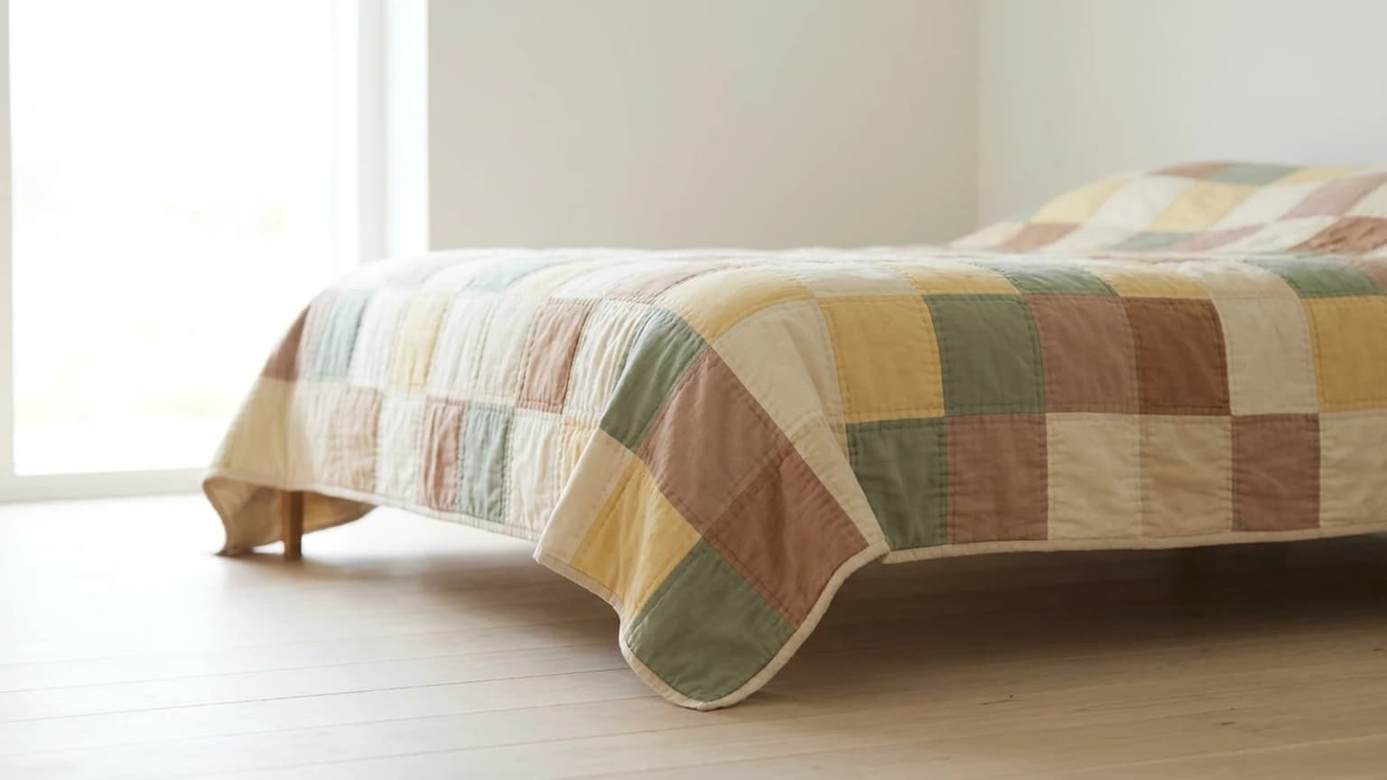 A patchwork quilt spread over a bed and hanging down the side, showing how far the finished quilt overhangs the mattress edge.